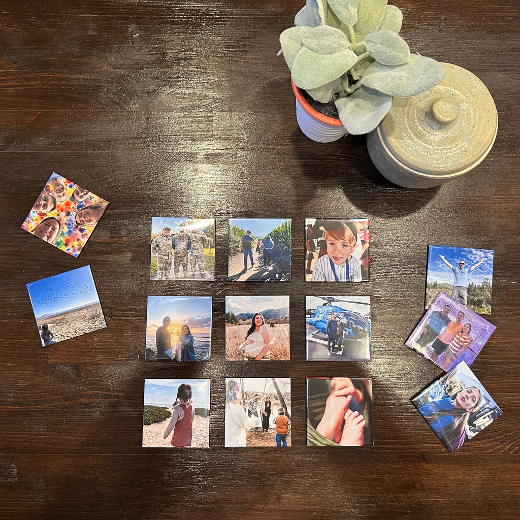 Small square memory magnets on a wooden table with a plant and photo album.