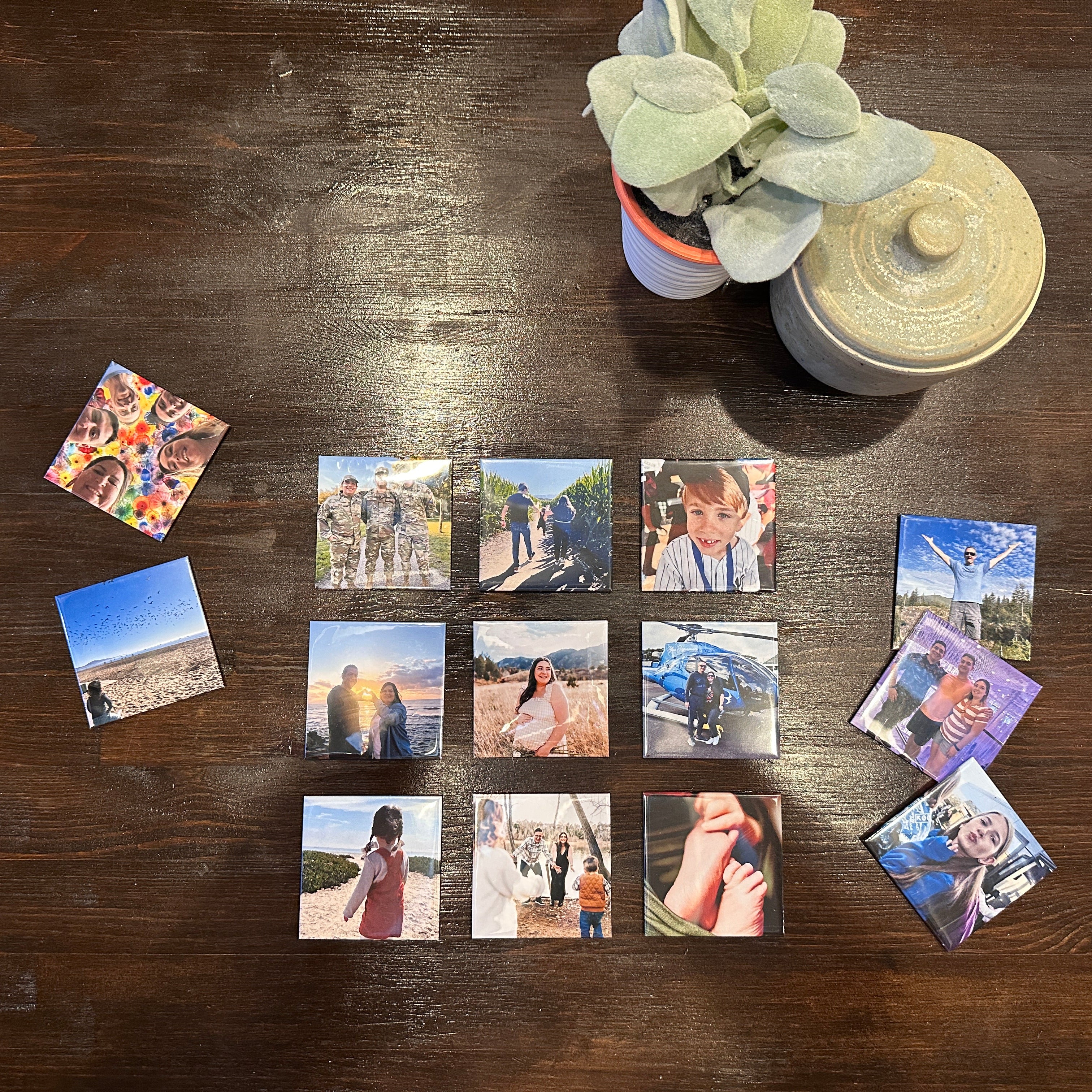 Small square memory magnets on a wooden table with a plant and photo album.