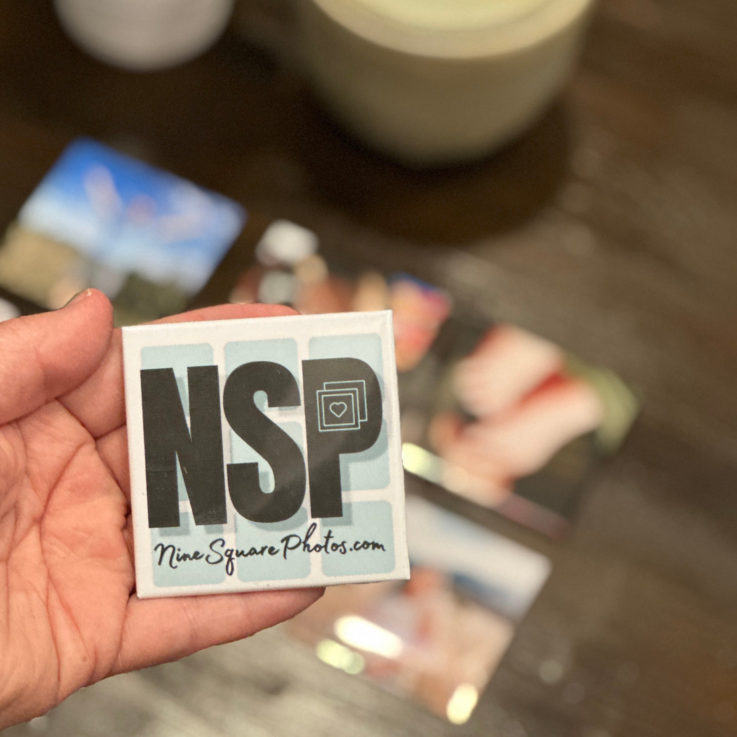 Hand holding a memory magmet 'NSP' and 'Nine Squire Photos' text on a photo magnet business card.